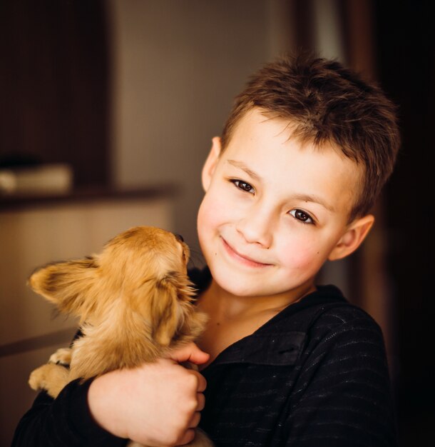 Happy boy holds little dog standing in the room