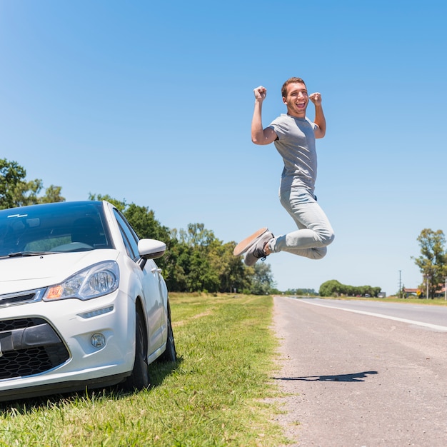 Счастливый мальчик прыгает на дороге рядом с автомобилем