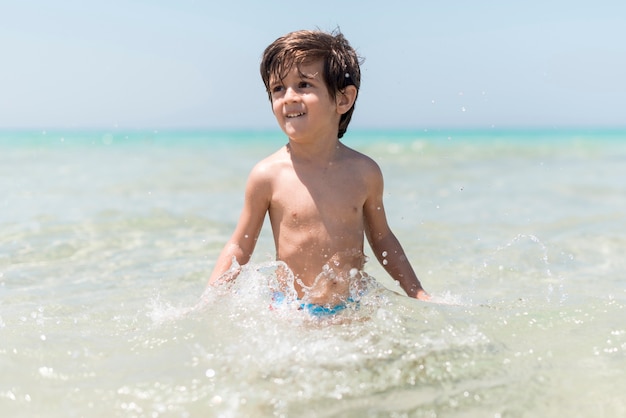 海辺で水で遊ぶ幸せな少年