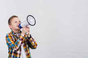 Free photo happy boy shouting through megaphone standing against white wall