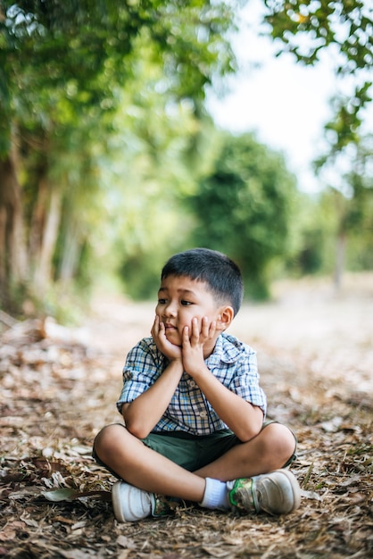 Free photo happy boy sitting and thinking alone in the park