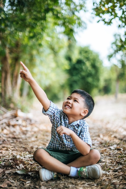 Foto gratuita ragazzo felice che si siede e che pensa da solo nel parco