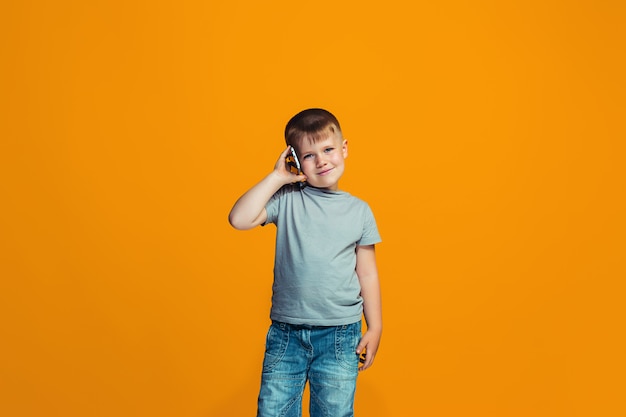 The happy boy standing and smiling against orange wall