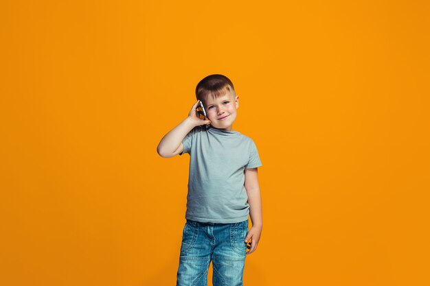 The happy boy standing and smiling against orange wall