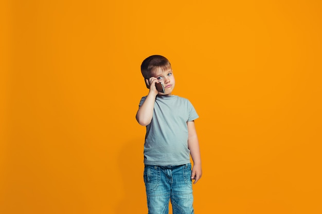 The happy boy standing and smiling against orange wall