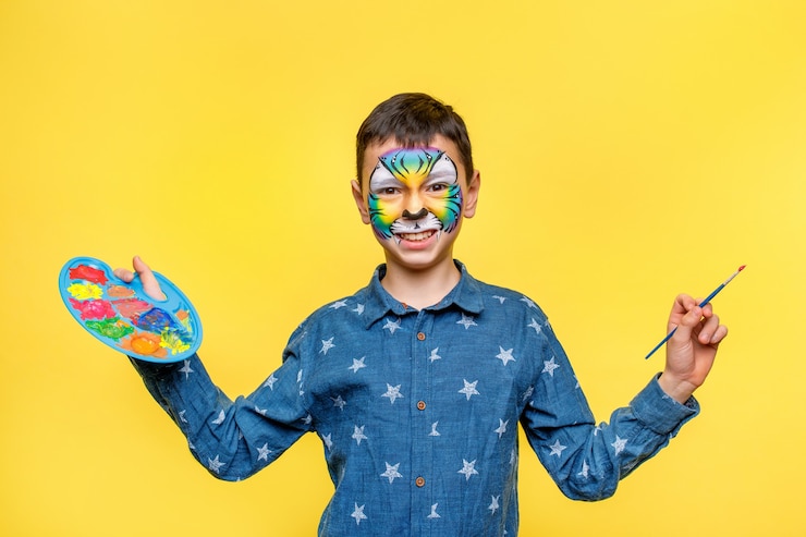 無料Photo 誕生日パーティーのペンキで幸せな少年、黄色の壁に分離されたガッシュとパレットを保持しているカラフルな虎。