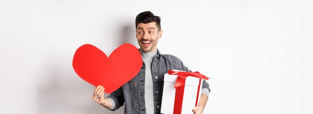 Foto gratuita fidanzato felice che fa regali romantici per la data di san valentino che tiene la scatola con il presente e il grande lui rosso