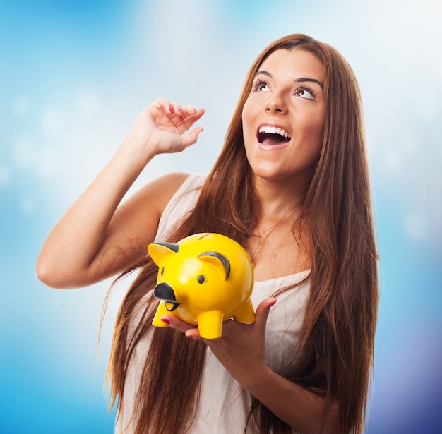 Happy brunette girl holding piglet moneybox.