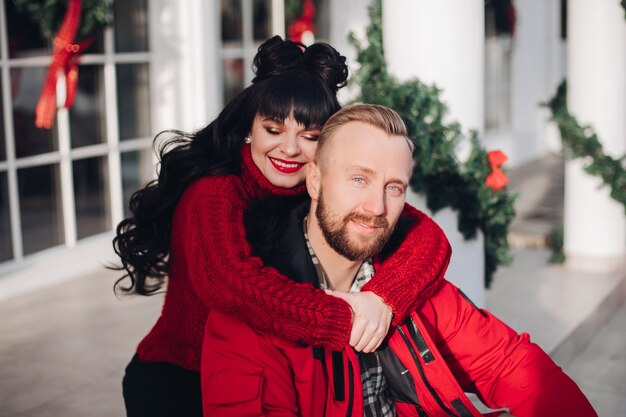 Happy brunette lady hugging her handsome boyfriend from behind near a pretty house