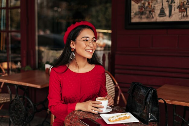 Happy brunette lady in red dress and beret smiles sincerely