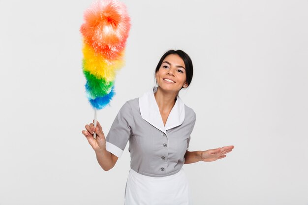 Happy brunette maid in gray uniform swipe with duster