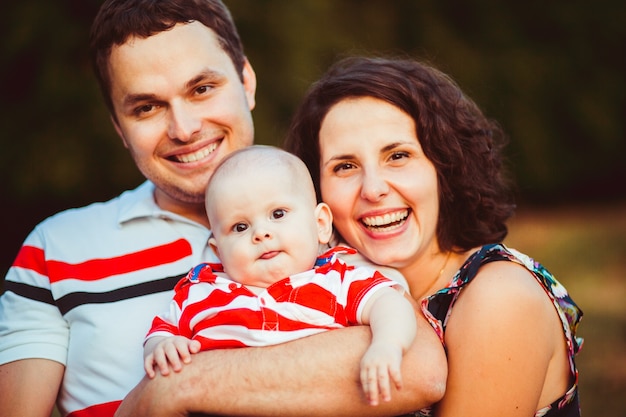 Happy brunette parents hold their little son in stripped shirt