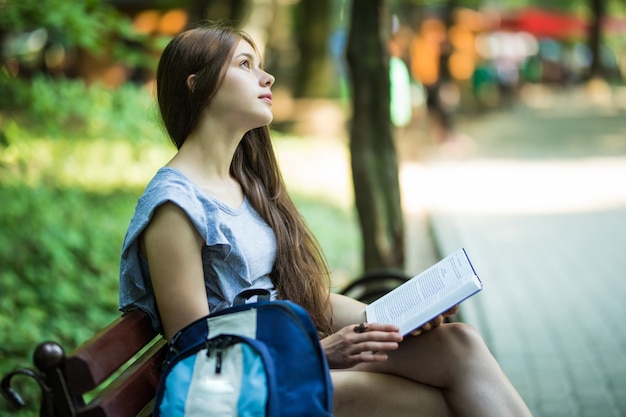 公園のベンチに座っている手にノートブックと幸せなブルネット