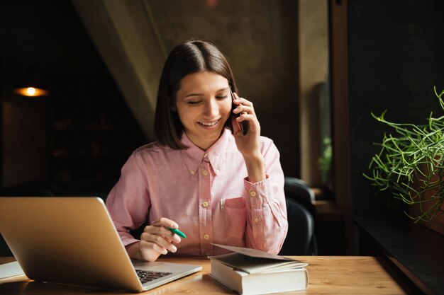 Happy brunette woman sitting by the table with laptop