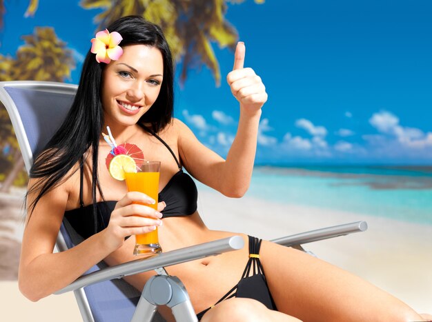 Happy brunette woman on vacation at beach with thumbs up sign