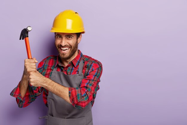 Happy builder wears construction helmet, does repairing with hammer