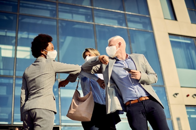 Felici colleghi di lavoro con maschere facciali che urtano il gomito mentre salutano all'aperto