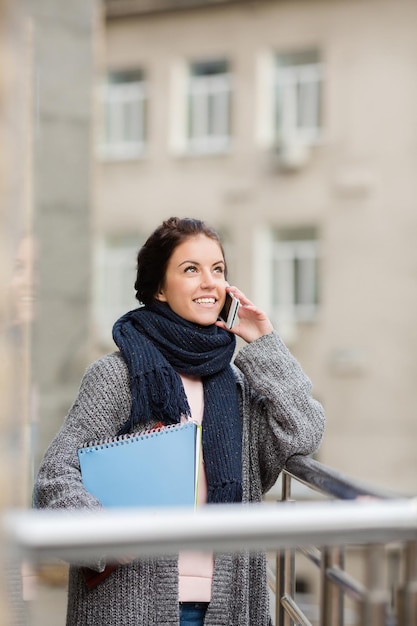 Free photo happy business lady busy talking over smartphone and looking away. beautiful lady standing on the street and holding documents.