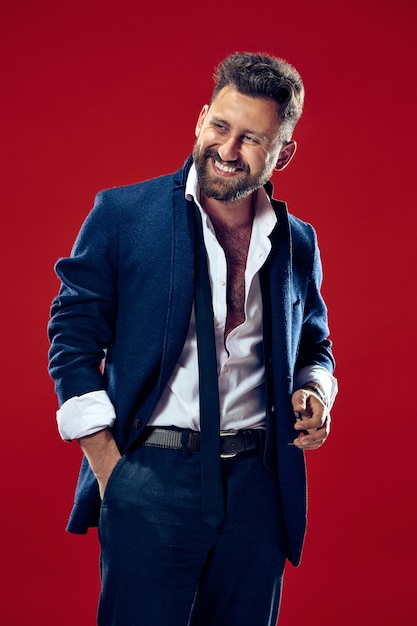 The happy business man standing and smiling against red wall.