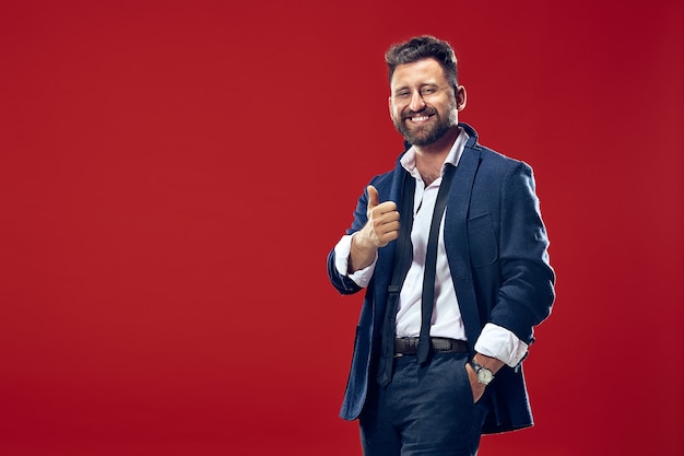 The happy business man standing and smiling against red wall