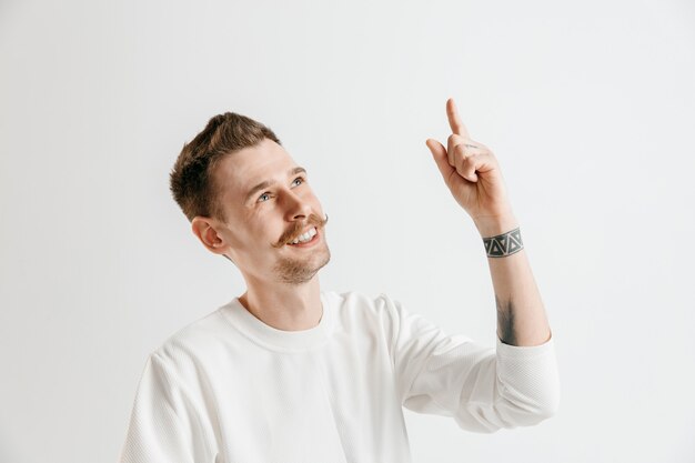 Happy business man standing, smiling isolated on gray studio background. Beautiful male half-length portrait. Young satisfy man pointing up. Human emotions, facial expression concept.