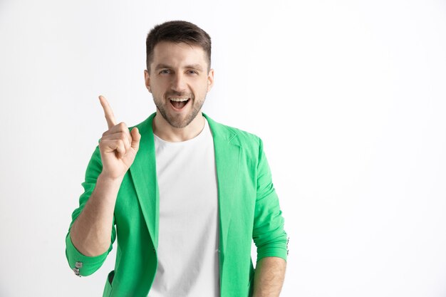 Happy business man standing, smiling and pointing up isolated on gray studio background. Beautiful male half-length portrait. Young satisfy man. Human emotions, facial expression concept.