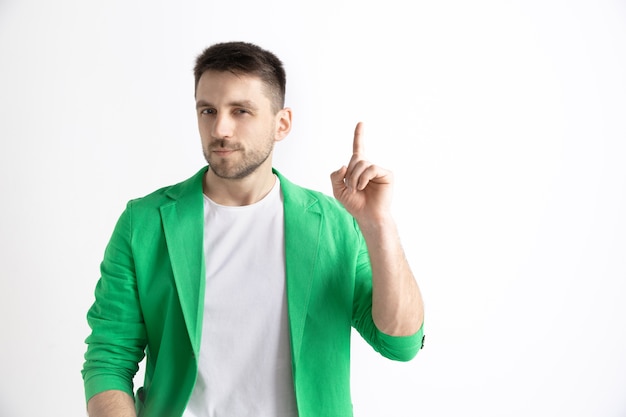 Happy business man standing, smiling and pointing up isolated on gray studio background. Beautiful male half-length portrait. Young satisfy man. Human emotions, facial expression concept.