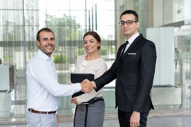 Happy business people shaking hands and looking at camera