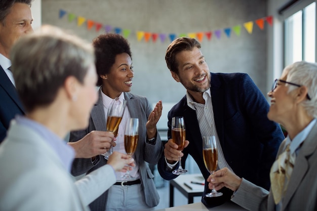 Free photo happy business team talking while drinking champagne at office party