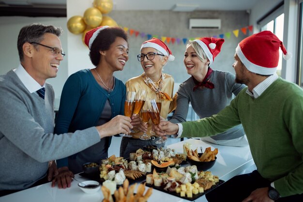 Счастливая бизнес-команда пьет шампанское на новогодней вечеринке в офисе