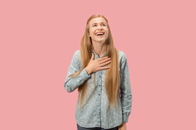 立っているとピンクのスタジオの背景に分離された笑顔幸せなビジネスの女性。美しい女性の半身像。若い感情的な女性。人間の感情、表情のコンセプト。正面図。