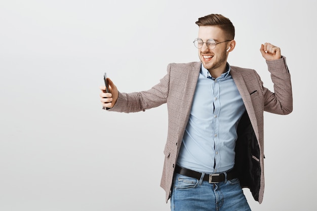 Happy businessman dancing in rejoice with smartphone, listening music in wireless earphones