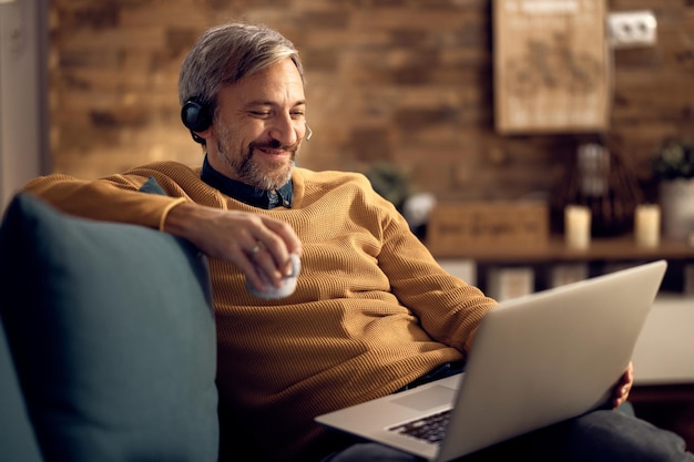 Счастливый бизнесмен пьет чай и пользуется ноутбуком вечером дома
