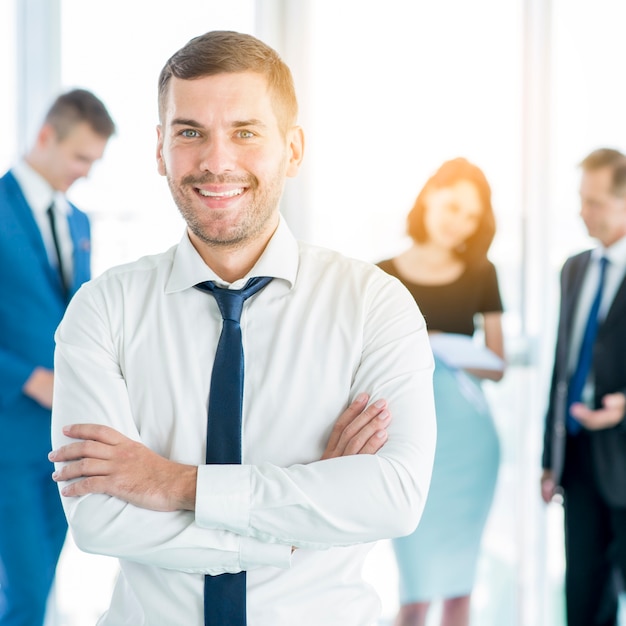 Happy businessman folding his arms with is colleagues in background