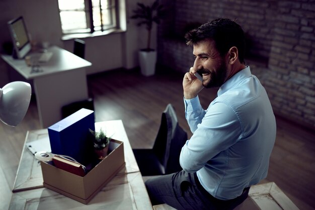 Happy businessman is talking on mobile phone during first day of his new job in the office