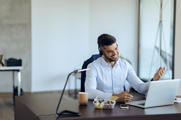 Счастливый бизнесмен делает видеозвонок через ноутбук во время работы в офисе