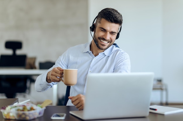 Happy businessman making video call while having coffee break in the office