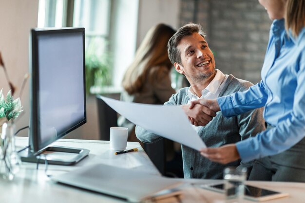 Happy businessman shaking hands with female colleague and congratulating her on excellent job she did