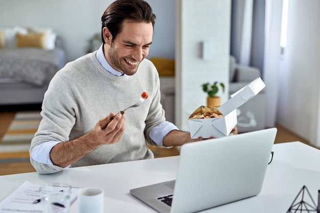 Happy businessman surfing the net on laptop during his lunch break at home