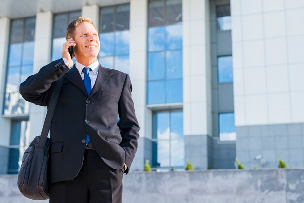 Happy businessman talking on smartphone in front of building