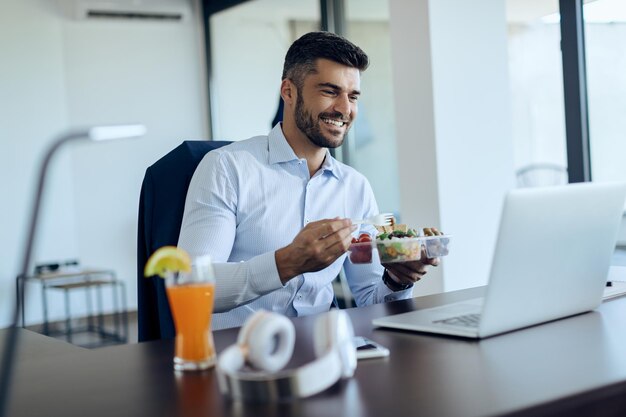 Счастливый бизнесмен использует ноутбук во время обеденного перерыва в офисе