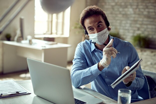 Happy businessman using laptop while having video conference at his office during coronavirus epidemic