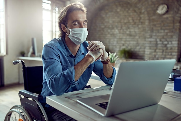 Free photo happy businessman in wheelchair wearing face mask while having video call over laptop in the office during virus epidemic