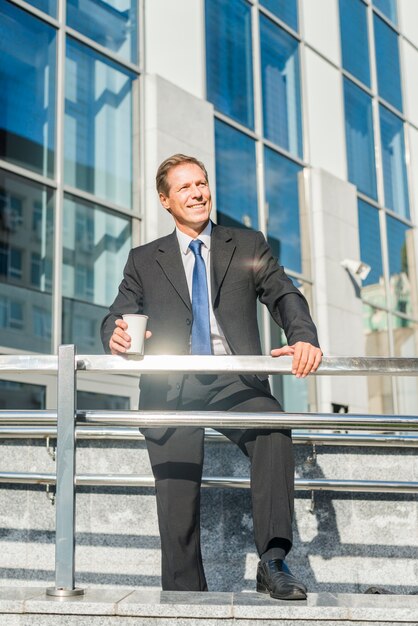 Happy businessman with cup of coffee standing in front of building