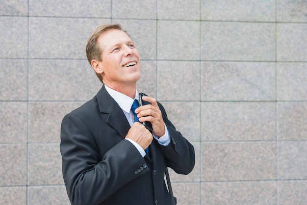 Happy businessman with mobile phone in front of tiled wall