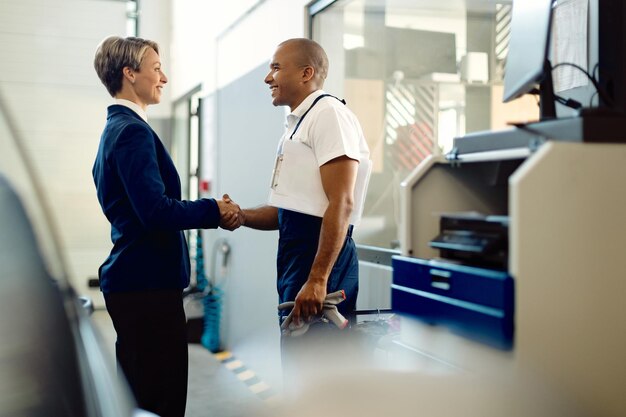 Happy businesswoman handshaking with African American mechanic at auto repair shop