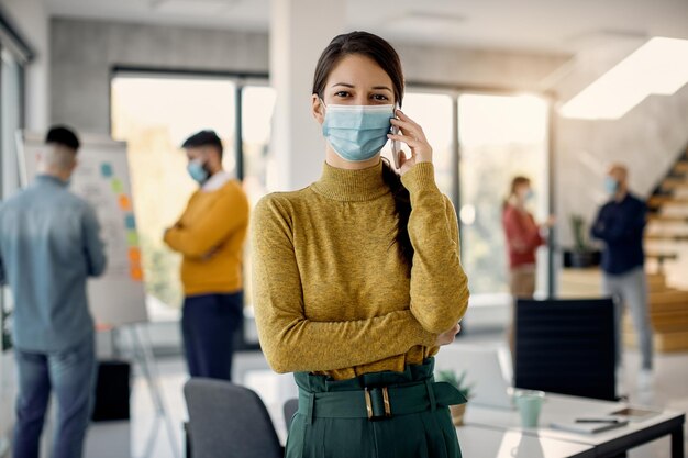 Happy businesswoman with protective face mask talking on the phone in the office