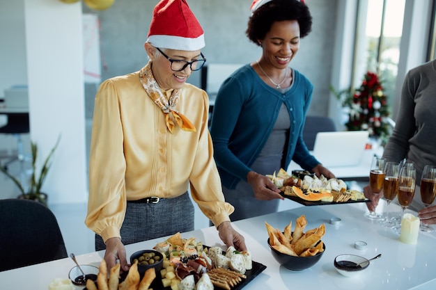 Happy businesswomen serving food while preparing for Christmas party in the office