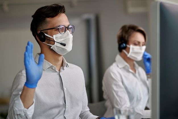 Happy call center agent waving while having video call with clients over desktop PC during coronavirus epidemic