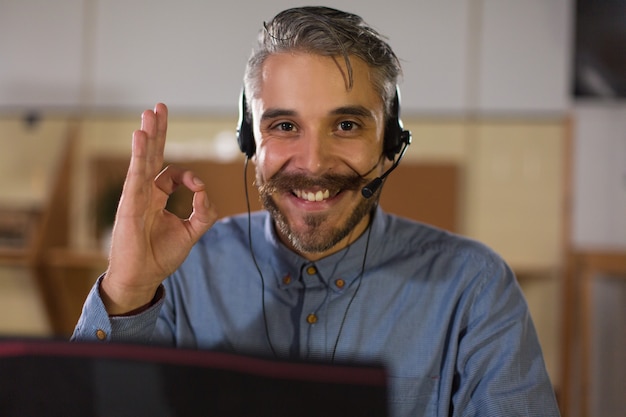 Operatore di call center felice che esamina macchina fotografica e che mostra segno giusto